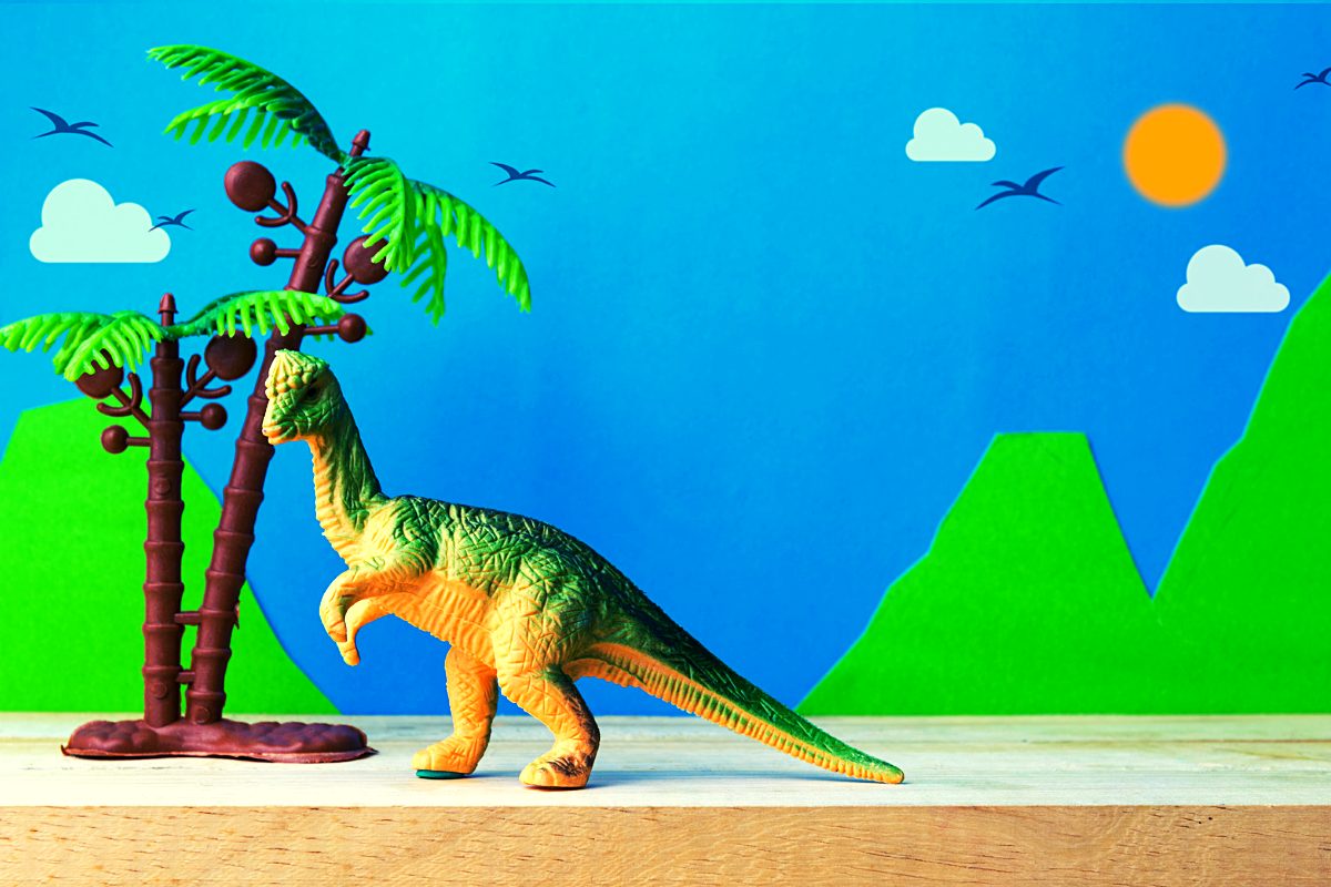 Dinosaur toys for kids- toy dinosaur next to tree with a volcano in the background