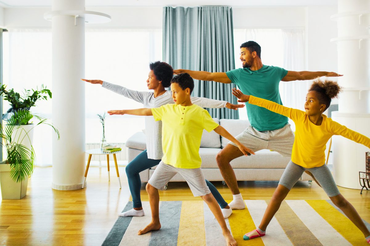 A family with mom, dad, son and daughter all doing yoga together in the living room.