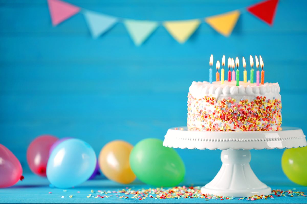 A cake with candles on it, birthday hat and birthday banner are all shown.